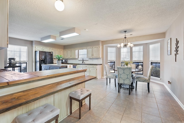 kitchen with pendant lighting, tile counters, black fridge, a chandelier, and cream cabinetry