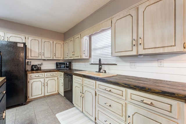 kitchen with light tile patterned floors, butcher block countertops, a textured ceiling, black appliances, and sink