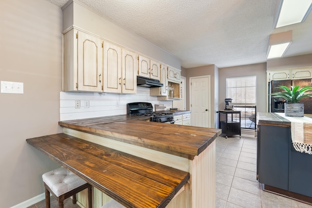 kitchen with a textured ceiling, black appliances, wooden counters, backsplash, and light tile patterned floors