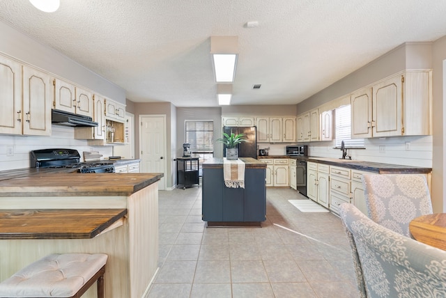 kitchen featuring a kitchen bar, a textured ceiling, black appliances, and cream cabinets