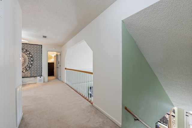 hallway with light colored carpet, vaulted ceiling, and a textured ceiling