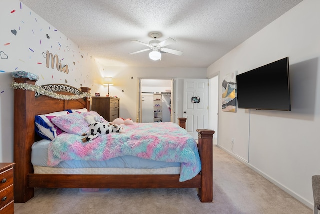 bedroom with light carpet, ceiling fan, a closet, a textured ceiling, and a walk in closet