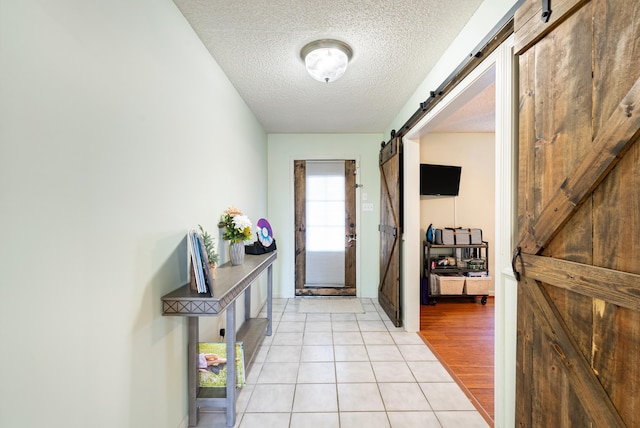 doorway with a textured ceiling, light tile patterned flooring, and a barn door