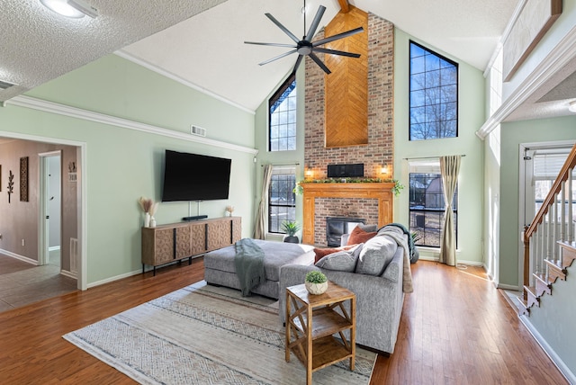 living room with a brick fireplace, wood-type flooring, high vaulted ceiling, and a textured ceiling