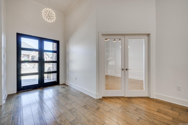 entryway featuring a notable chandelier, light wood-type flooring, a towering ceiling, french doors, and ornamental molding