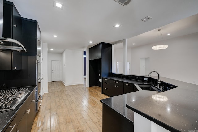 kitchen with decorative light fixtures, stainless steel gas stovetop, dark stone countertops, light hardwood / wood-style floors, and sink