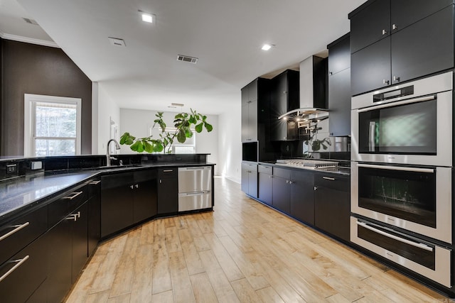 kitchen featuring wall chimney range hood, appliances with stainless steel finishes, sink, and light hardwood / wood-style flooring