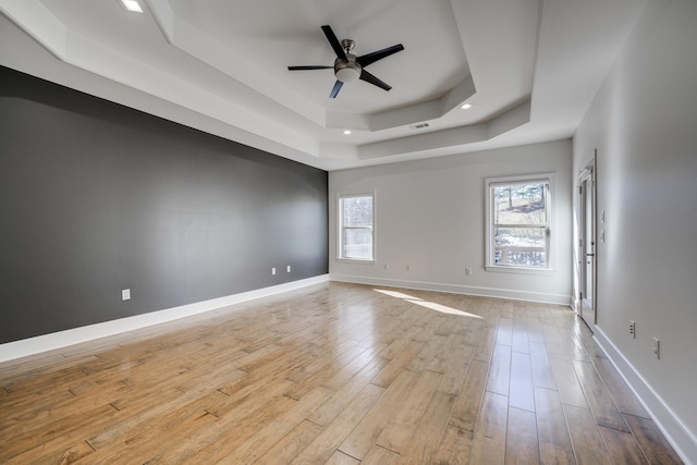 empty room with ceiling fan, a raised ceiling, and light wood-type flooring