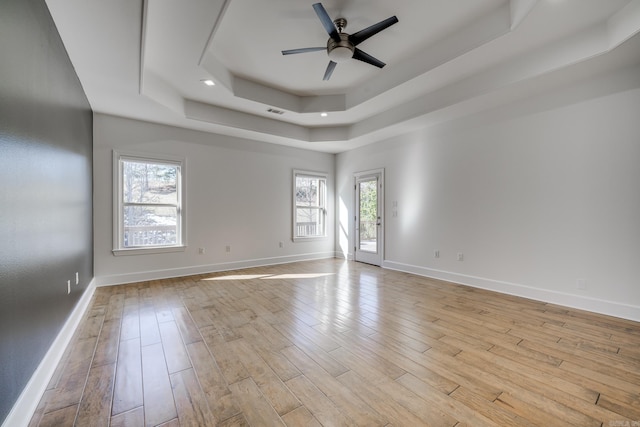 empty room featuring a raised ceiling, ceiling fan, and light hardwood / wood-style flooring