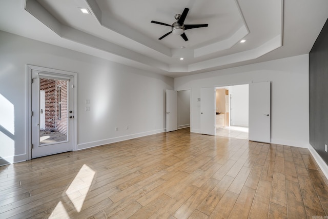 empty room with ceiling fan, light hardwood / wood-style flooring, and a raised ceiling