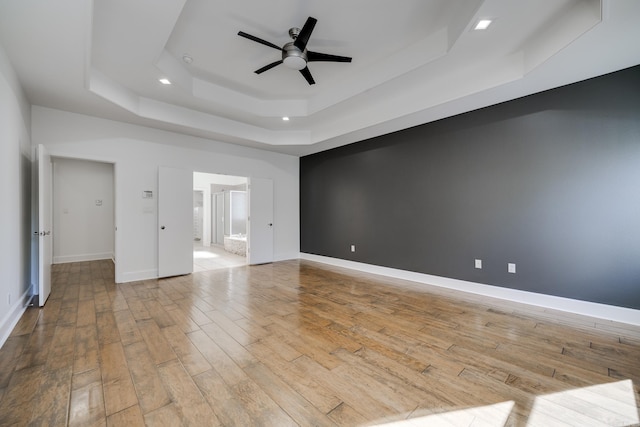 empty room featuring ceiling fan, a tray ceiling, and light hardwood / wood-style floors