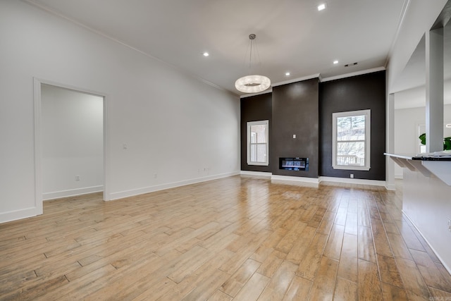 unfurnished living room with light wood-type flooring, a fireplace, an inviting chandelier, and ornamental molding