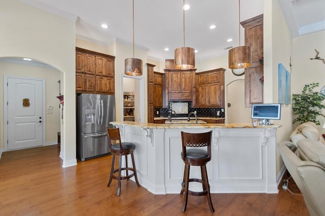 kitchen with stainless steel fridge with ice dispenser, backsplash, hanging light fixtures, light stone countertops, and a breakfast bar