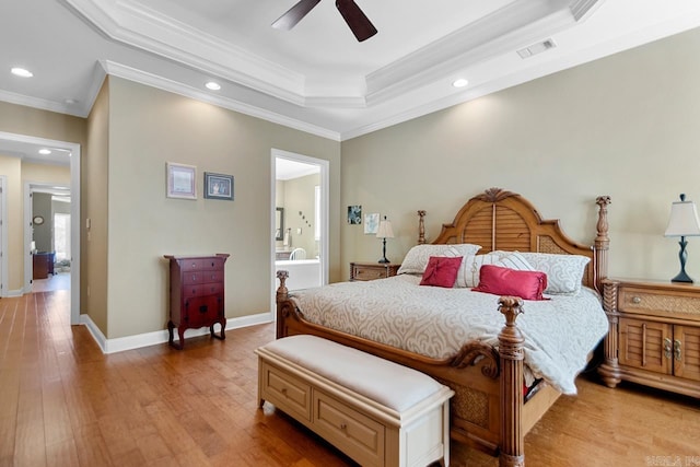 bedroom featuring ceiling fan, ensuite bath, a raised ceiling, crown molding, and light hardwood / wood-style flooring