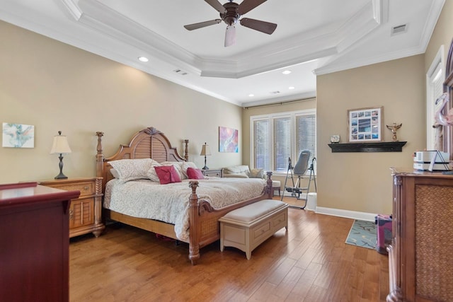 bedroom featuring ceiling fan, crown molding, wood-type flooring, and a tray ceiling