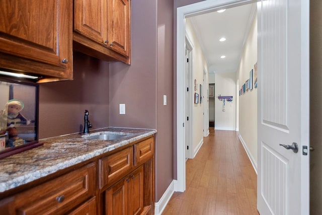 bar with light stone counters, sink, light hardwood / wood-style flooring, and crown molding