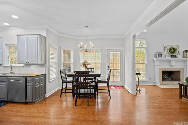 dining space featuring a fireplace, sink, a chandelier, crown molding, and light wood-type flooring