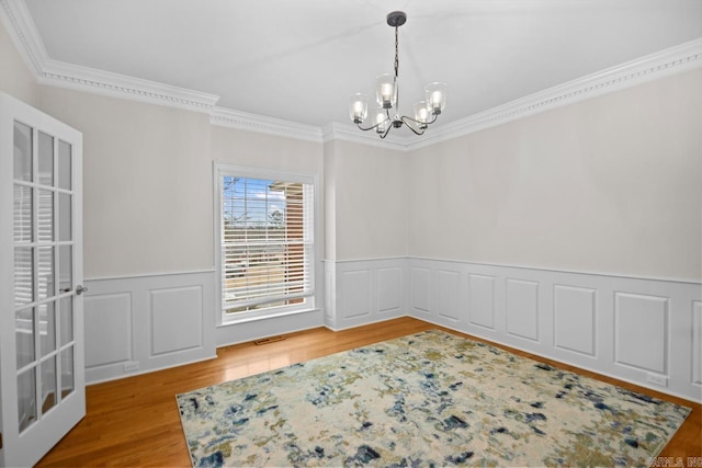 unfurnished room featuring hardwood / wood-style flooring, crown molding, and an inviting chandelier