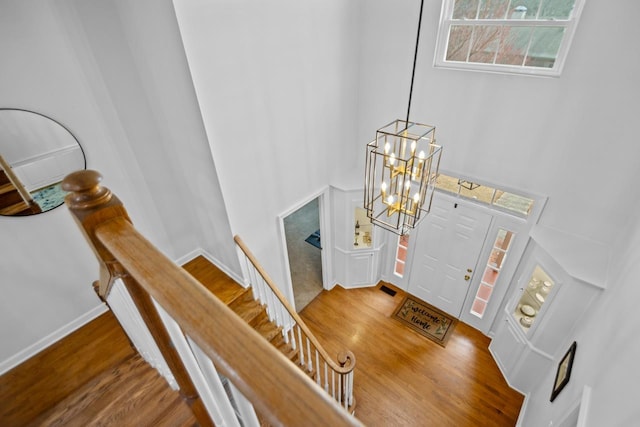 foyer entrance with a towering ceiling, hardwood / wood-style floors, and a notable chandelier