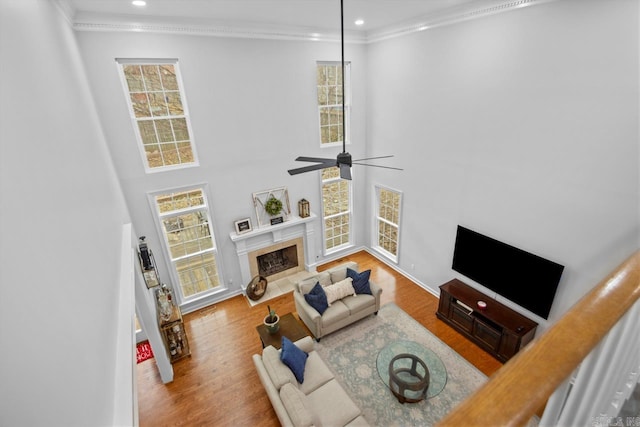 living room with hardwood / wood-style flooring, crown molding, ceiling fan, and a fireplace