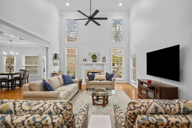 living room featuring crown molding, a tile fireplace, a wealth of natural light, light hardwood / wood-style floors, and ceiling fan with notable chandelier