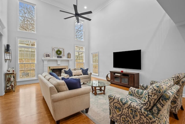 living room with ceiling fan, ornamental molding, a tiled fireplace, and light wood-type flooring