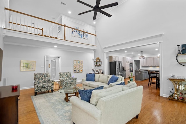 living room with a high ceiling, ceiling fan, and light hardwood / wood-style flooring