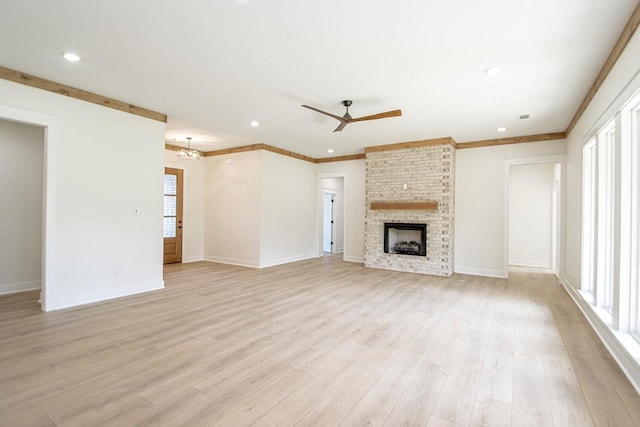 unfurnished living room with a brick fireplace, a wealth of natural light, ceiling fan with notable chandelier, and light hardwood / wood-style flooring