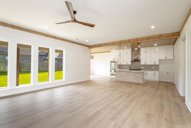 unfurnished living room with ceiling fan, beamed ceiling, and light hardwood / wood-style flooring