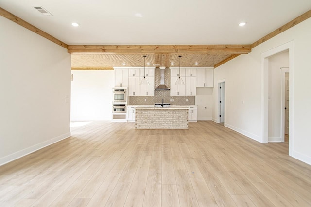 unfurnished living room featuring beam ceiling, sink, and light hardwood / wood-style flooring