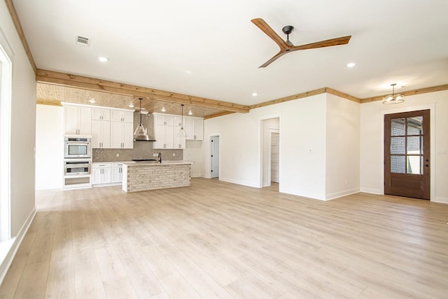 unfurnished living room with ceiling fan, beamed ceiling, and light wood-type flooring