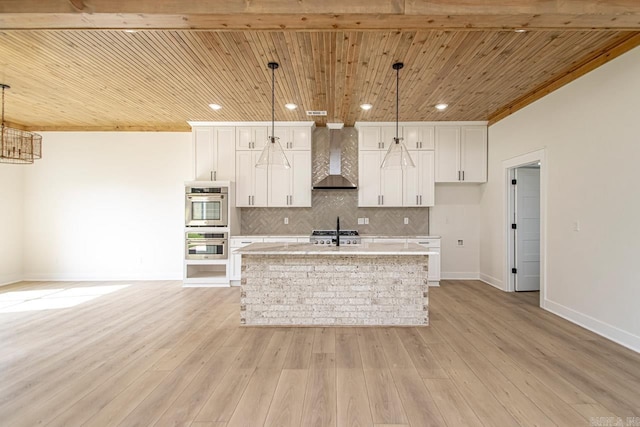 kitchen with a kitchen island with sink, light hardwood / wood-style floors, hanging light fixtures, and wall chimney range hood