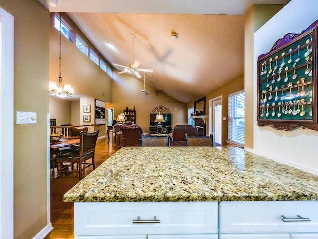 kitchen with white cabinetry, ceiling fan with notable chandelier, light stone counters, and decorative light fixtures