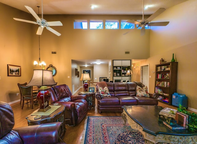 living room with ceiling fan with notable chandelier, a high ceiling, and hardwood / wood-style flooring