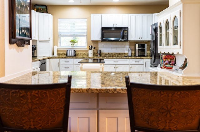 kitchen with white cabinetry, kitchen peninsula, backsplash, fridge, and light stone counters