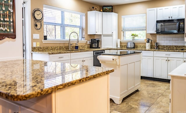 kitchen featuring a center island, black appliances, white cabinets, light stone counters, and sink