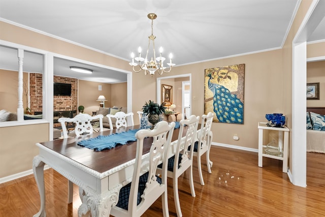 dining area with a brick fireplace, hardwood / wood-style flooring, ornamental molding, and a notable chandelier