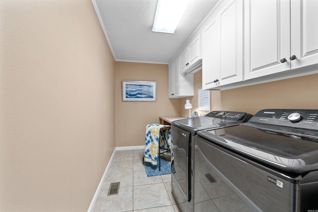 washroom featuring crown molding, washing machine and clothes dryer, a textured ceiling, light tile patterned floors, and cabinets