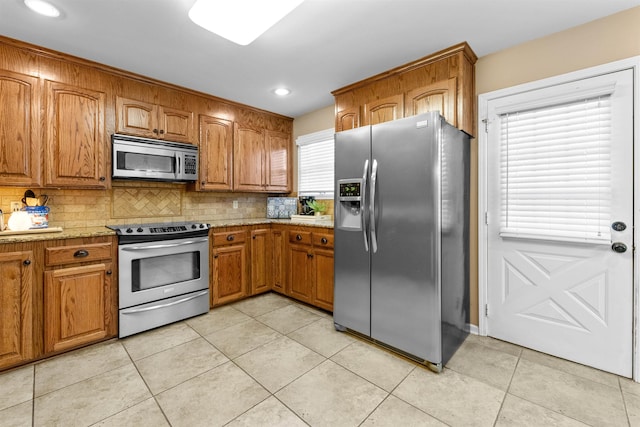 kitchen with tasteful backsplash, appliances with stainless steel finishes, light tile patterned flooring, and light stone counters