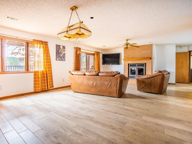 unfurnished living room with ceiling fan, a textured ceiling, a fireplace, and light hardwood / wood-style flooring