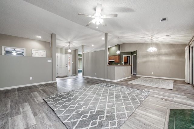 unfurnished living room with lofted ceiling, ceiling fan with notable chandelier, a textured ceiling, and hardwood / wood-style flooring