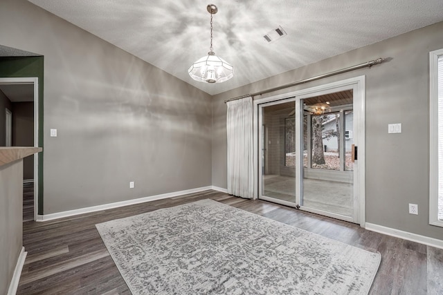 empty room with dark wood-type flooring, a notable chandelier, a textured ceiling, and lofted ceiling