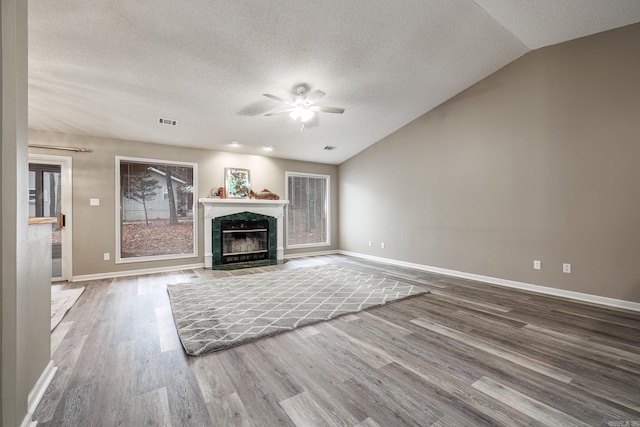 unfurnished living room featuring hardwood / wood-style flooring, ceiling fan, lofted ceiling, a textured ceiling, and a high end fireplace