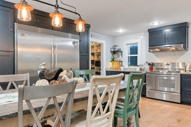 kitchen with hanging light fixtures, decorative backsplash, appliances with stainless steel finishes, and light hardwood / wood-style floors