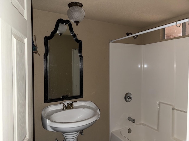 bathroom with a textured ceiling, tub / shower combination, and sink