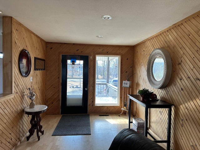 entrance foyer featuring light wood-type flooring, an inviting chandelier, and wooden walls