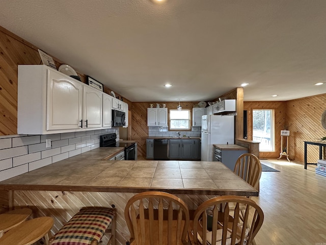 kitchen featuring black appliances, kitchen peninsula, tile counters, and white cabinetry