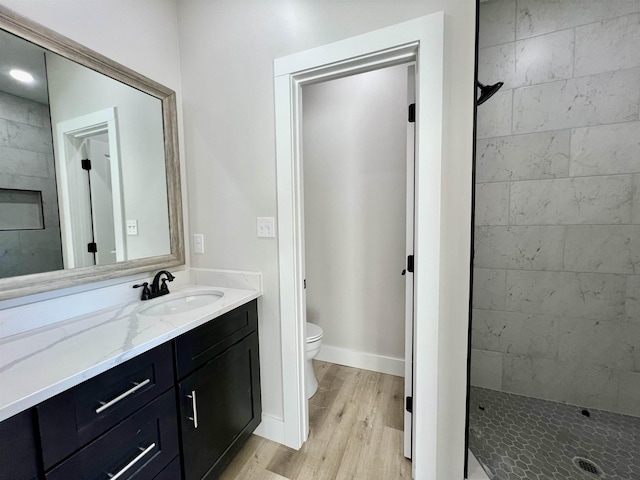 bathroom with hardwood / wood-style floors, toilet, vanity, and a tile shower