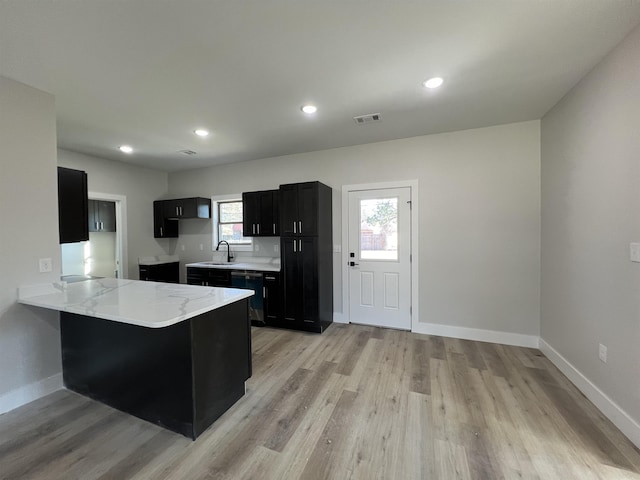 kitchen featuring light wood-type flooring, kitchen peninsula, light stone countertops, and sink