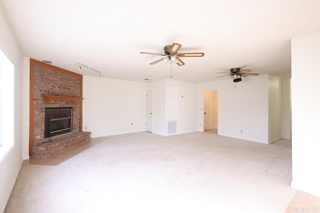 unfurnished living room with a brick fireplace, rail lighting, light colored carpet, and ceiling fan